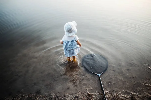 彼女の隣に漁網、湖で水に立って小さな幼児の女の子の背面図. — ストック写真