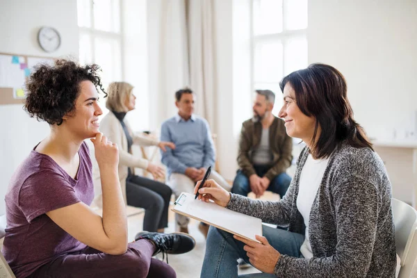 Seniorberater mit Klemmbrett im Gespräch mit einer Frau während der Gruppentherapie. — Stockfoto