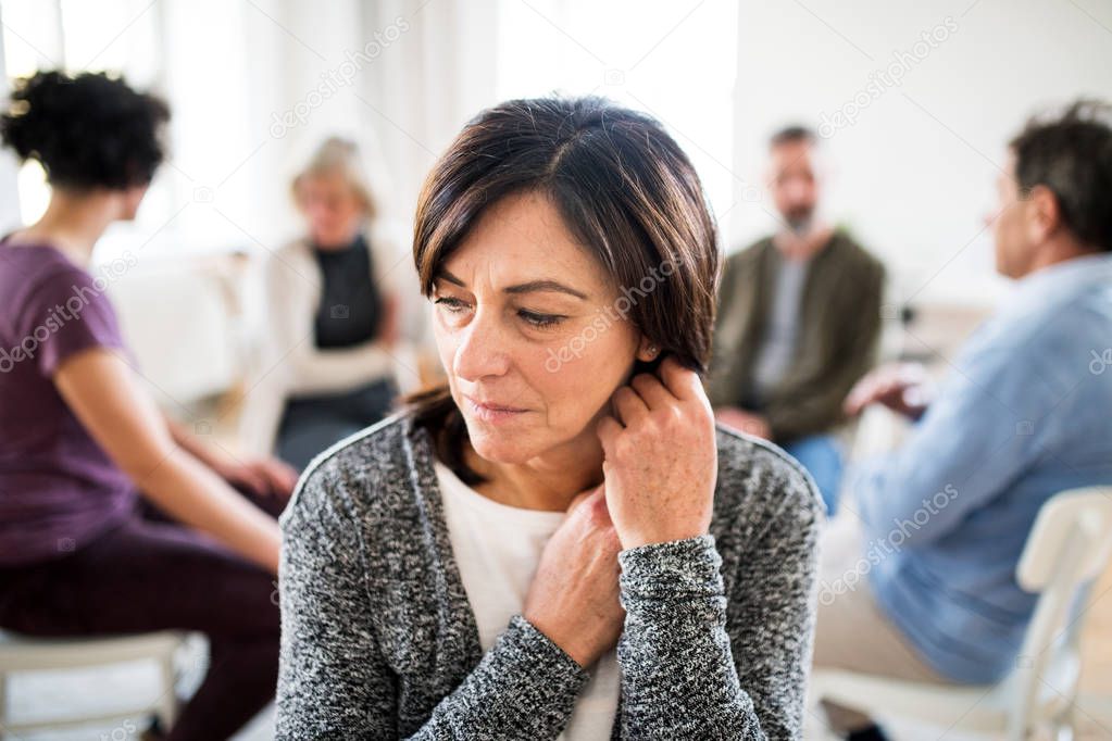 Portrait of senior depressed woman during group therapy.