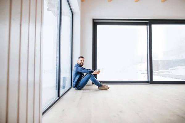 Un homme mature assis sur le sol dans une maison neuve non meublée, tenant du café . — Photo