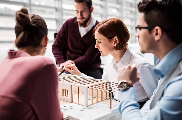 Skupina mladých architektů s modelem domu stojícího v úřadu, mluví. — Stock fotografie