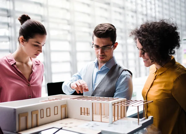 Group of young architects with model of a house standing in office, talking. — Stock Photo, Image