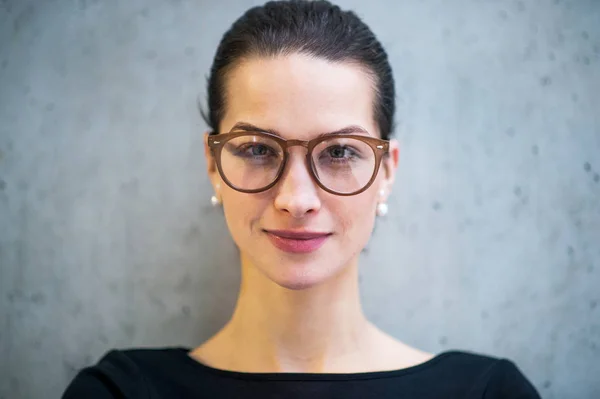 Porträt einer jungen Geschäftsfrau mit Brille, die im Büro steht und in die Kamera blickt. — Stockfoto