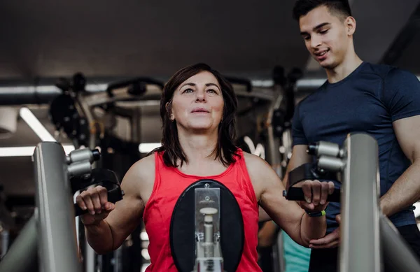 Une femme senior avec un jeune entraîneur faisant de l'exercice de musculation dans la salle de gym . — Photo