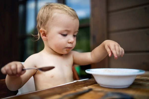 Petite fille debout près d'une table sur un patio en été, mangeant de la soupe . — Photo