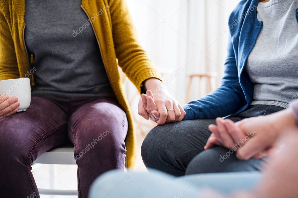 Midsection of men and women sitting in a circle during group therapy.