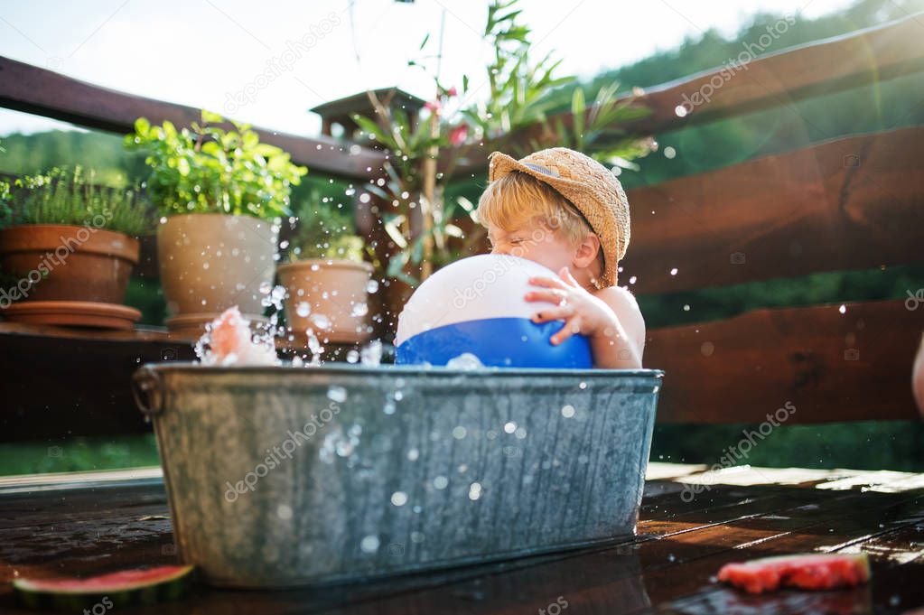 Small boy with a ball in bath outdoors in garden in summer, playing in water.