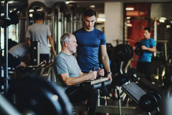 Un uomo anziano con un giovane allenatore che fa esercizio di allenamento di forza in palestra . — Foto Stock