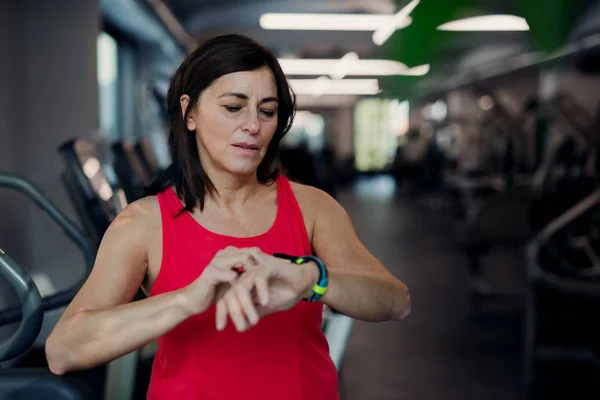 En äldre kvinna i gym vila efter gör övning, kontroll tid. — Stockfoto