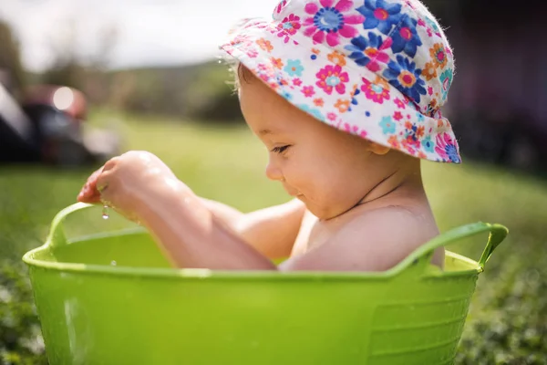 Klein meisje met hoed in emmer buiten in de tuin in de zomer spelen in water. — Stockfoto
