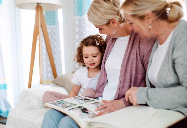 Een klein meisje met moeder en grootmoeder thuis, kijken naar foto 's. — Stockfoto