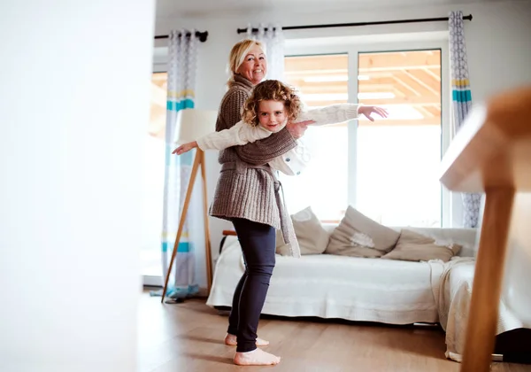 Um retrato de menina pequena com avó se divertindo em casa . — Fotografia de Stock