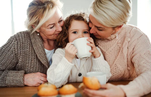 Um retrato de menina pequena com mãe e avó na mesa em casa . — Fotografia de Stock