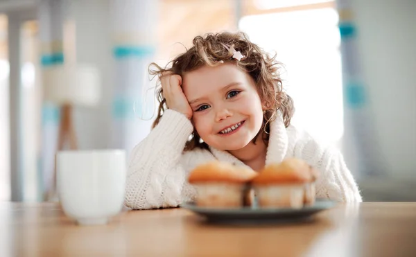 Portrait d'une petite fille assise à la table à la maison, mangeant des muffins . — Photo