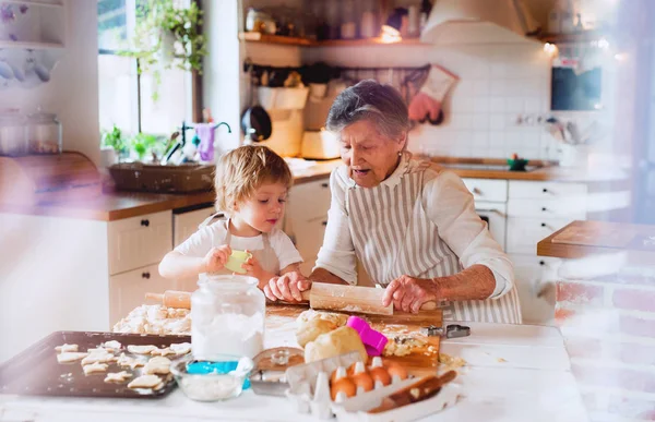 Senior grandmother with small toddler boy making cakes at home. — Stock Photo, Image