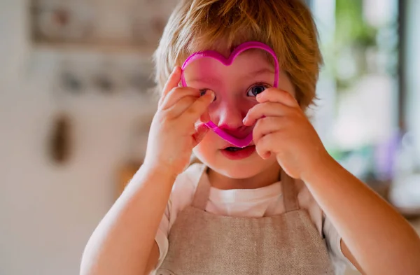 Un niño pequeño mirando a través de un cortador de pasteles en casa . — Foto de Stock