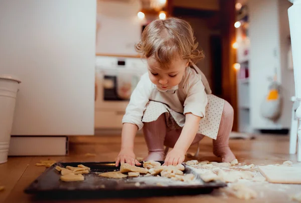 A small toddler girl making cakes on the floor in the kitchen at home. — Stock Photo, Image