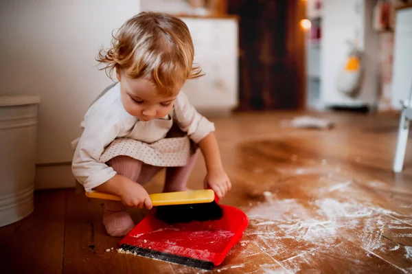 Malé batole dívka s kartáčem a lopatku zametal podlahu v kuchyni doma. — Stock fotografie