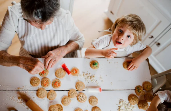 A top view of senior grandmother with small toddler boy making cakes at home. — Stock Photo, Image
