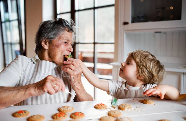 Senior nonna con piccolo bambino ragazzo fare e mangiare torte a casa . — Foto Stock