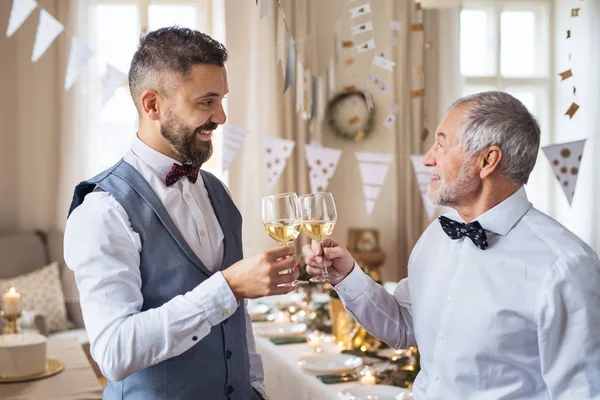 En senior och mogen man stå inomhus i ett rum för en part, spottar glasögon. — Stockfoto