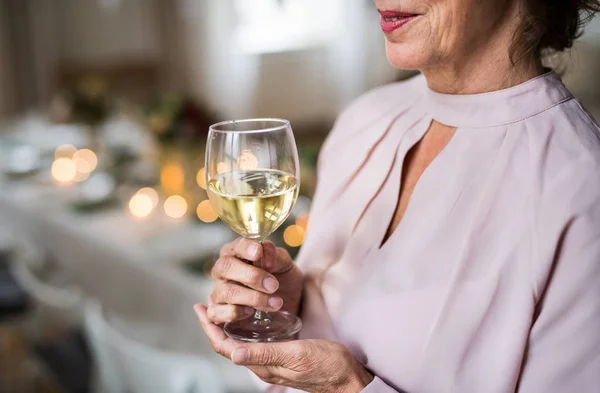 Ein Mittelteil einer älteren Frau, die drinnen in einem Raum steht, der für eine Party eingerichtet ist, Wein in der Hand. — Stockfoto