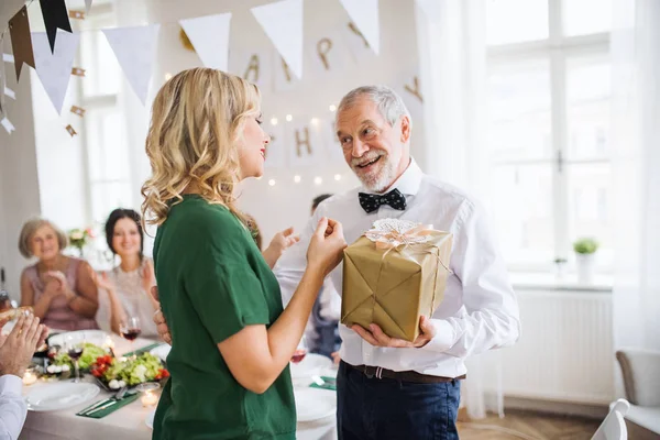 Jovem mulher dando um presente para seu avô em festa indoor . — Fotografia de Stock