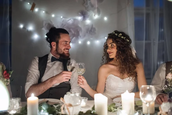 A young couple sitting at a table on a wedding, clinking glasses. — Stock Photo, Image