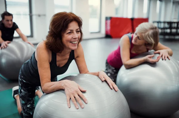 Grupp av glada kvinnliga seniorer i gymmet gör övning på passa bollar. — Stockfoto