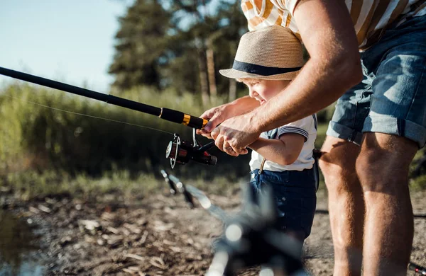 Ein mittlerer Teil des Vaters mit einem kleinen Jungen, der an einem See fischt. — Stockfoto