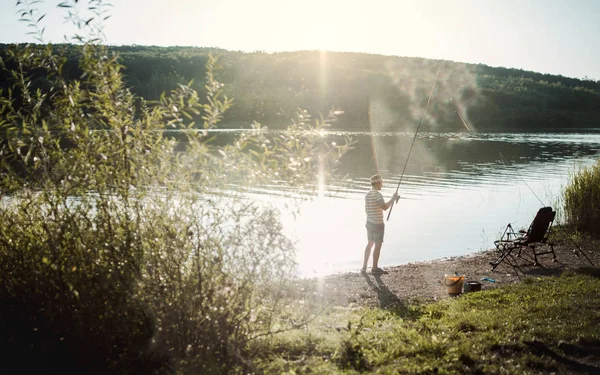 En bakre vy av en mogen man fiske vid en sjö, håller en stav. — Stockfoto