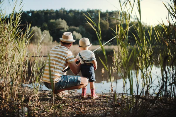 Una vista trasera de padre maduro con un pequeño hijo pequeño al aire libre pesca junto a un lago . —  Fotos de Stock