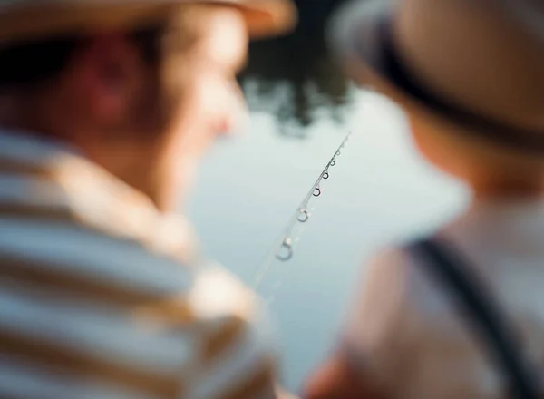 Una vista trasera de padre maduro con un pequeño hijo pequeño al aire libre pesca junto a un lago . —  Fotos de Stock