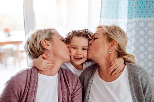 Un retrato de niña pequeña con madre y abuela en casa, besándose . — Foto de Stock