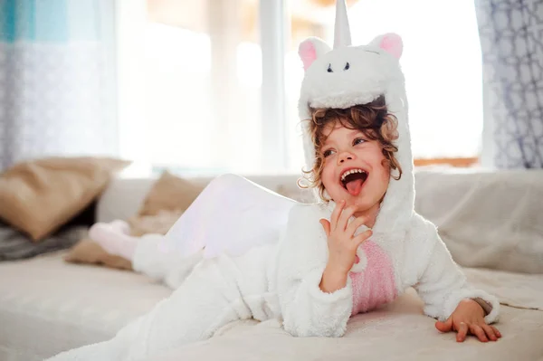 Un retrato de niña pequeña con máscara de unicornio acostada en el sofá en casa . — Foto de Stock