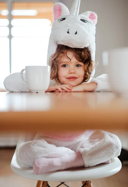 Portret mała dziewczynka w jednorożca maska siedzi przy stole w domu. — Zdjęcie stockowe