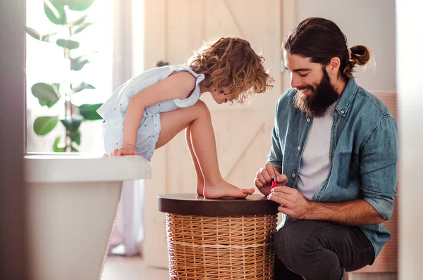 Jovem pai pintando pequenas filhas unhas em um banheiro em casa . — Fotografia de Stock