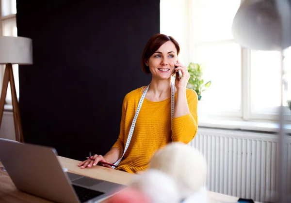 Mujer creativa joven en un estudio, usando un teléfono inteligente. Una puesta en marcha de negocio de sastrería . —  Fotos de Stock