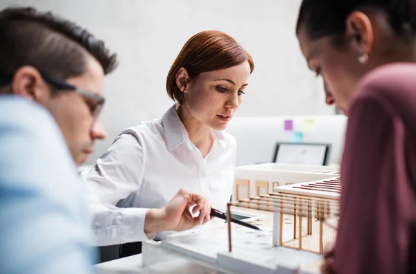 Group of young architects with model of a house standing in office, talking. — Stock Photo, Image