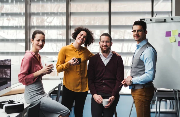 Een groep van jonge ondernemers met kopje koffie staande in kantoor. — Stockfoto
