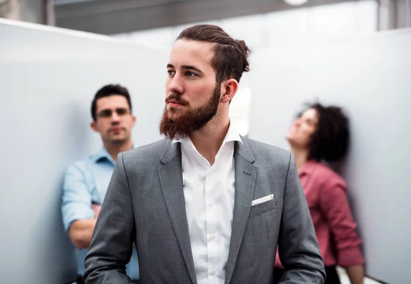 En ung affärsman i kostym stående i office, kollegor i bakgrunden. — Stockfoto