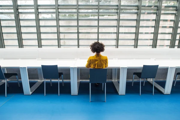 Visão traseira de jovem estudante ou empresária sentado na mesa em um quarto em uma biblioteca ou escritório . — Fotografia de Stock