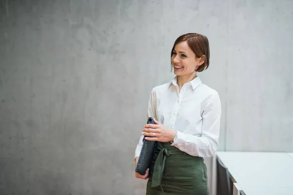 Porträt einer jungen Geschäftsfrau, die mit Laptoptasche im Büro steht. — Stockfoto