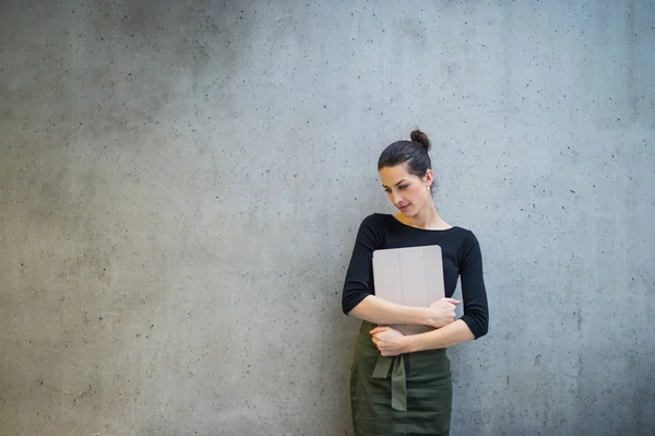 Wanita bisnis muda dengan tablet berdiri menghadap dinding beton di kantor . — Stok Foto