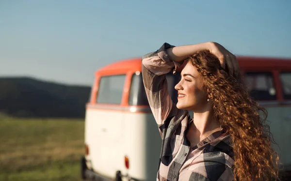 Une jeune fille en voyage à travers la campagne, debout près d'une minifourgonnette . — Photo