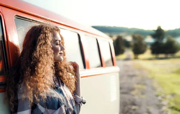 Una giovane ragazza in viaggio in campagna, appoggiata a un minivan . — Foto Stock