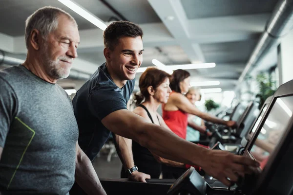 Un gruppo di anziani in palestra con un giovane allenatore che fa esercizio cardio . — Foto Stock