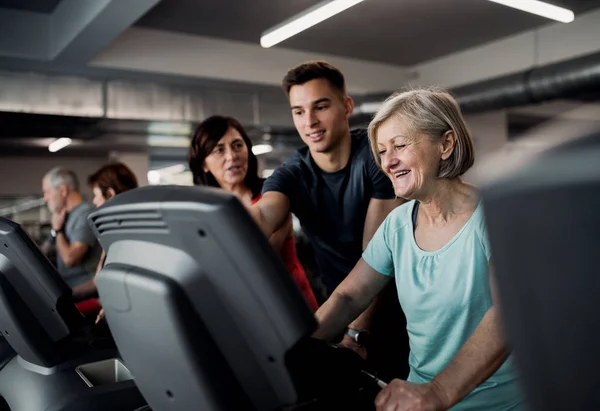 Un grupo de personas mayores en el gimnasio con un joven entrenador haciendo ejercicio cardiovascular . — Foto de Stock