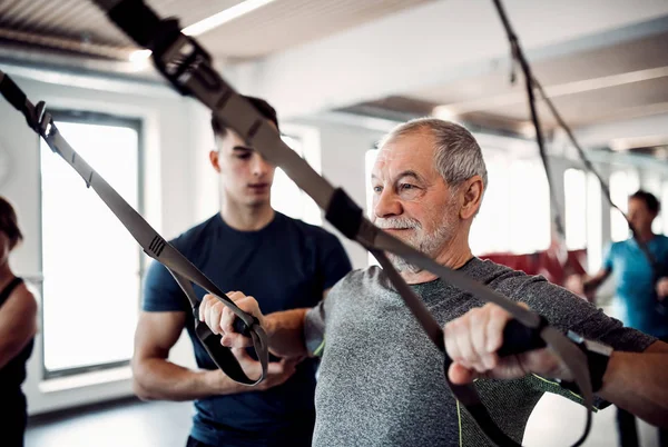 Un groupe de personnes âgées en salle de gym avec un jeune entraîneur faisant de l'exercice avec TRX . — Photo