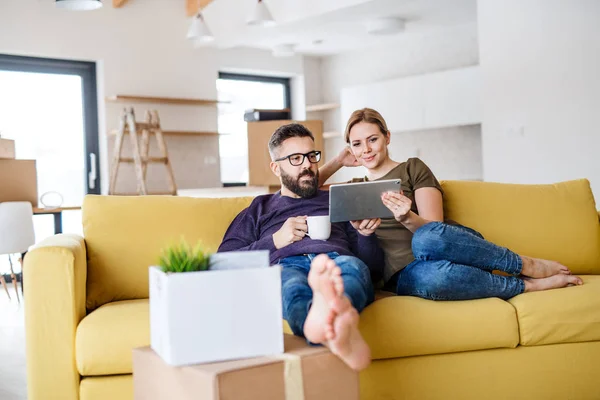 Ein junges Paar mit Tablet und Kaffee sitzt auf dem Sofa und zieht in ein neues Zuhause. — Stockfoto